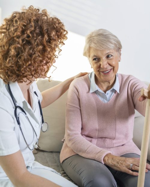 Friendly relationship between smiling caregiver in uniform and happy elderly woman. Supportive young nurse looking at senior woman. Young caring lovely caregiver and happy ward